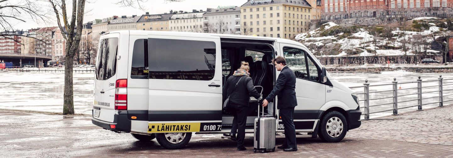 Taksinkuljettaja avustaa matkustajan matkatavaroineen kyytiin.