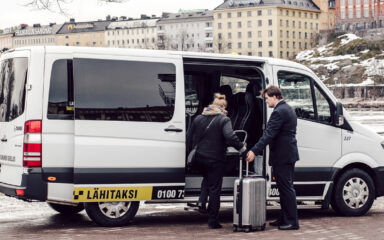 Taksinkuljettaja avustaa matkustajan matkatavaroineen kyytiin.